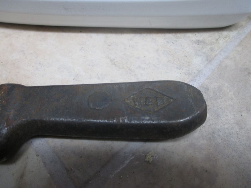 Close-up of a rusty metal tool with a diamond-shaped stamp that reads 'W.C.D.'