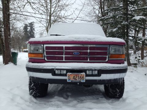 1992 Ford F-150 - A maroon 1992 Ford F-150 truck sits covered in snow during winter, showing its front grille and headlights.