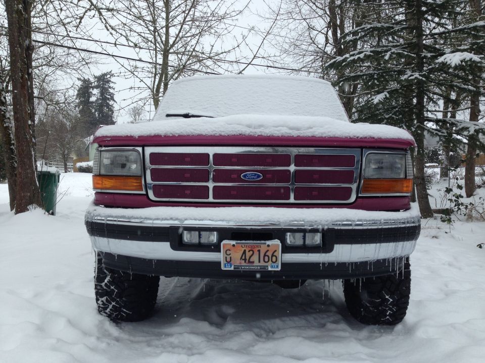 1992 Ford F-150 truck covered in snow, front view, maroon grille with Ford emblem