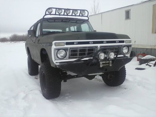 Dark green 1978 Ford Bronco with a roof rack and aftermarket bumper in snow