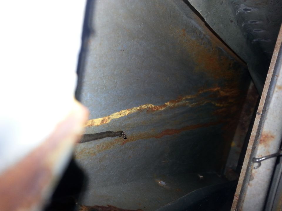 close-up of rusted metal channel with orange streaks, part of a vehicle's interior structure