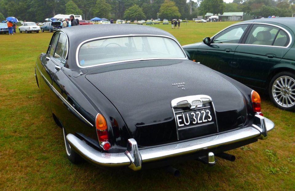 Black Jaguar 420 G with EU 3223 license plate, parked on grass next to a green car