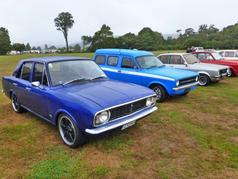 1969 MINI Cooper - A blue Ford sedan and a blue van are parked on a grassy field at an outdoor car show.