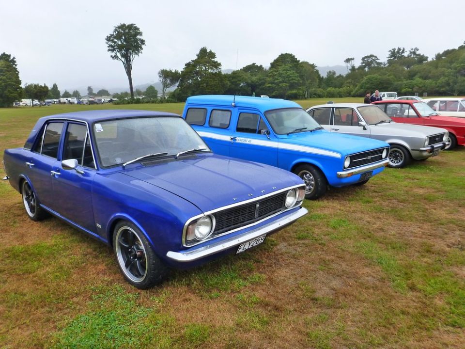 Blue Ford sedan with aftermarket wheels, parked next to a blue van