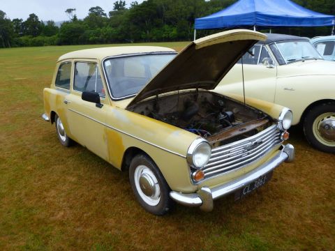 1969 MINI Cooper - A yellow station wagon sits on grass with its hood open, parked next to another vehicle under a blue tent.