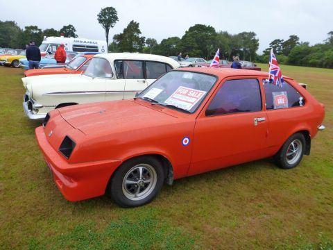 1969 MINI Cooper - An orange hatchback car is parked on grass with other vehicles and an ambulance in the background.