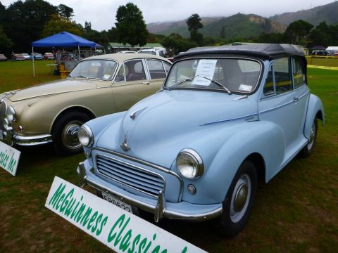 1969 MINI Cooper - Two classic cars are parked on a grassy field under an overcast sky, with hills in the background.