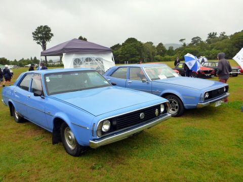 1969 MINI Cooper - Two blue sedans are parked on a grassy field, possibly at a car show.