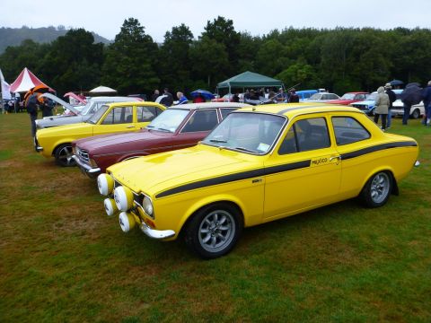 1969 MINI Cooper - A yellow Ford Escort Mexico is parked on grass at an outdoor car show with other vehicles.