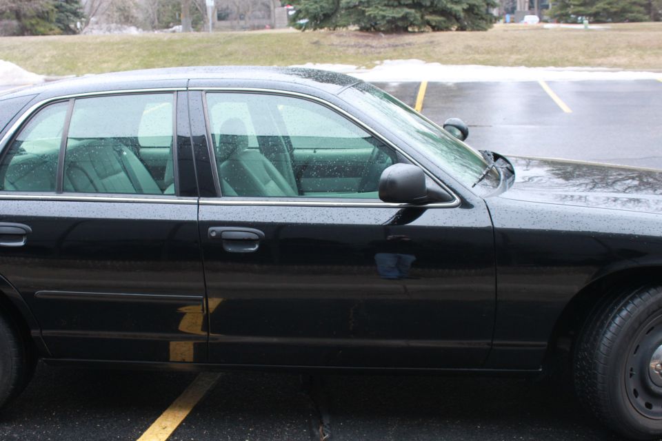 Side view of a black 2005 Ford Crown Victoria with tinted windows and a police spotlight