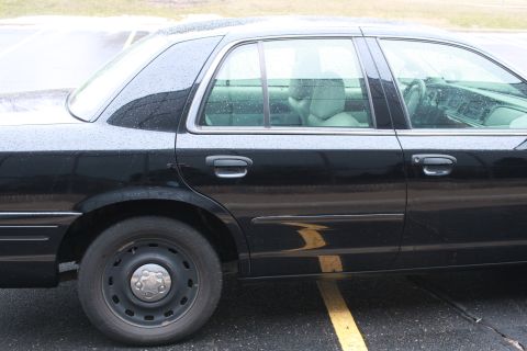 2005 Ford Crown Victoria - This black sedan is seen from the side, parked on a wet surface with yellow lines on the ground.