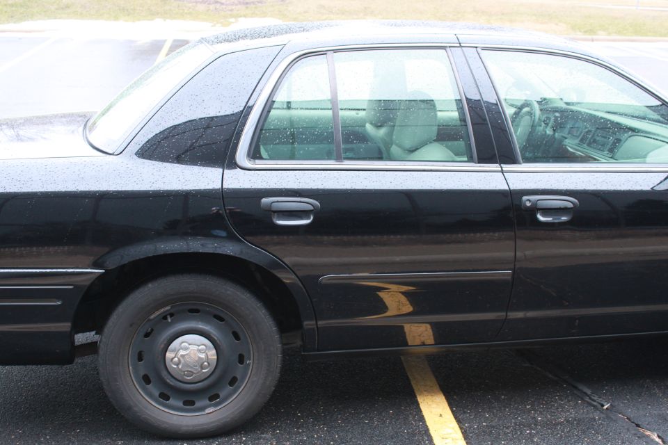 Side view of a black sedan with steel wheels parked on wet pavement