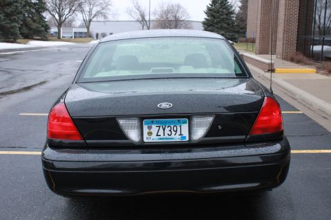 2005 Ford Crown Victoria - Rear view of a black 2005 Ford Crown Victoria parked in a lot on a cloudy day.