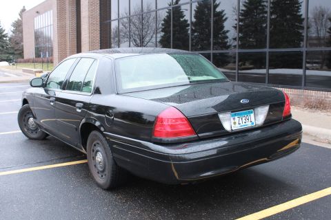 2005 Ford Crown Victoria - Rear view of a black 2005 Ford Crown Victoria sedan parked outside a building.