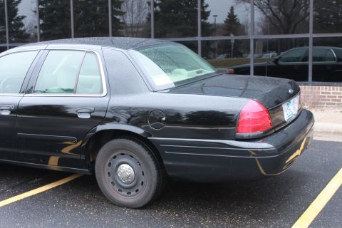 2005 Ford Crown Victoria - The rear quarter panel of a black sedan is visible, parked next to a building with reflective windows.