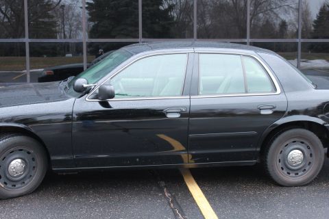 2005 Ford Crown Victoria - A black 2005 Ford Crown Victoria sedan is parked next to a building, with another vehicle visible in the reflection.