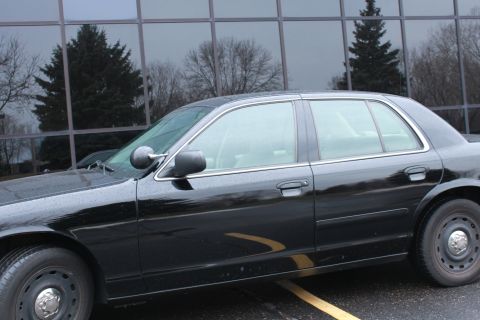 2005 Ford Crown Victoria - A black sedan is parked in front of a building with reflective windows, showing trees in the background.