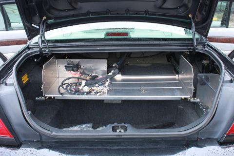 2005 Ford Crown Victoria - The open trunk of a car reveals custom aluminum shelving and a complex wiring harness, obscuring the original vehicle year.