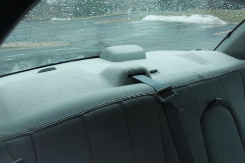 2005 Ford Crown Victoria - The rear interior of a vehicle with a seatbelt visible, seen through a rain-streaked window.