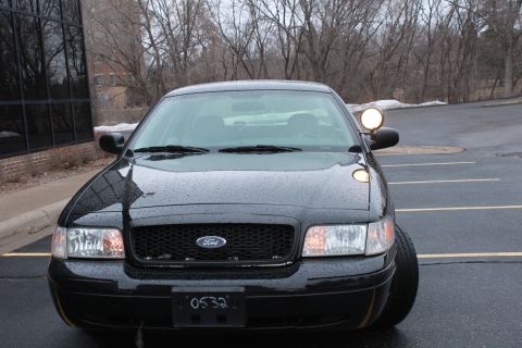 2005 Ford Crown Victoria - Black 2005 Ford Crown Victoria police car parked outside a building on a rainy day.