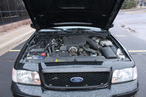 2005 Ford Crown Victoria - The engine bay of a black 2005 Ford Crown Victoria is visible with the hood raised, revealing the engine and front grille.