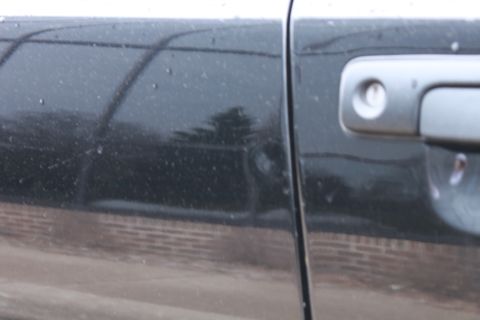 2005 Ford Crown Victoria - Detail of a car's side door and handle, showing water droplets on the black paint.