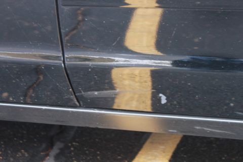 2005 Ford Crown Victoria - The lower body panel of a vehicle shows wear and tear, with a yellow reflection visible.
