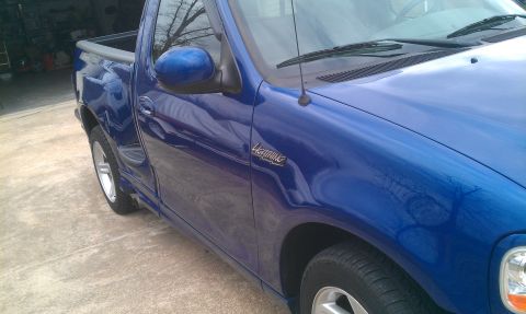 2003 Ford F-150 - A blue Ford F-150 Lightning pickup truck is parked outside on a concrete surface. The 'Lightning' badge is visible on the fender.