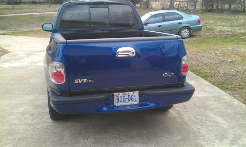 2003 Ford F-150 - Rear view of a blue 2003 Ford F-150 SVT Lightning pickup truck parked on a driveway, with another car in the background.
