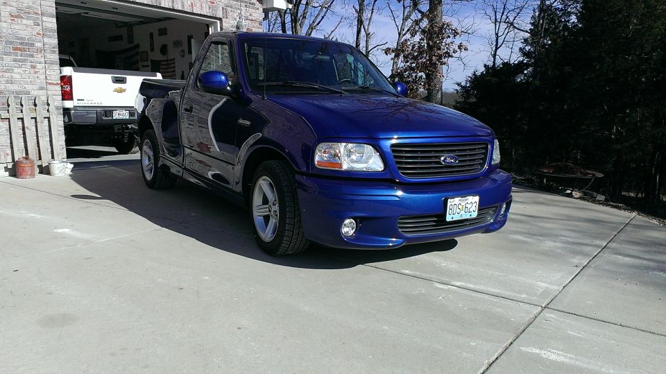 Blue 2003 Ford F-150 Lightning pickup truck parked in driveway, white Chevrolet Silverado in garage behind it