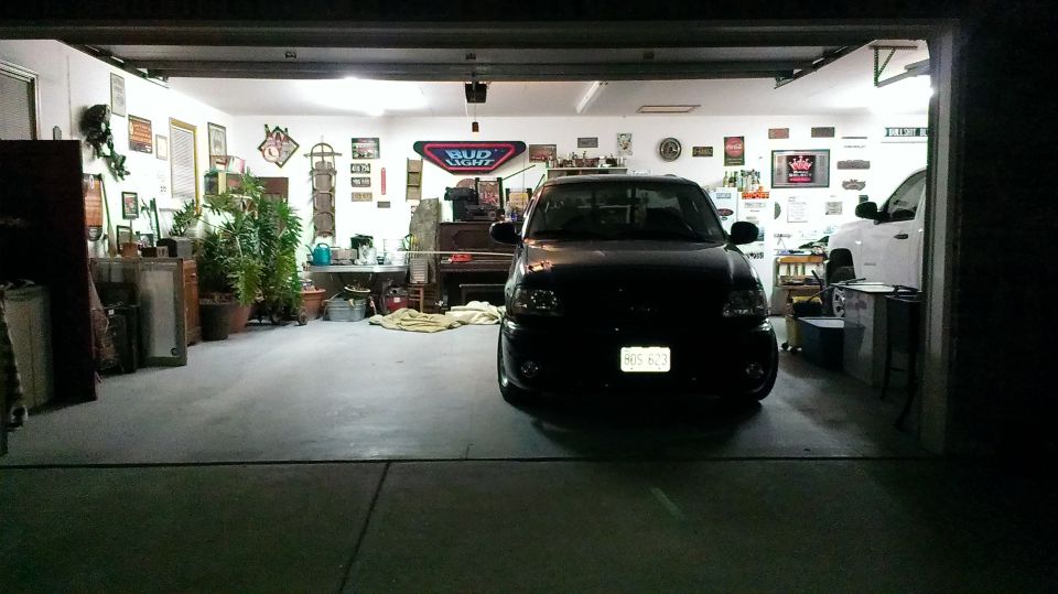 Black pickup truck parked in a garage with a white truck behind it. License plate is visible