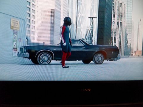 1994 Jeep Cherokee - A person in a superhero costume walks past a black coupe in an urban setting.