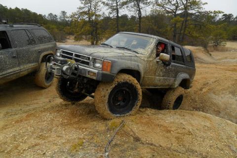 1987 Toyota 4Runner - Two SUVs navigate a muddy off-road course, kicking up dirt as they go.