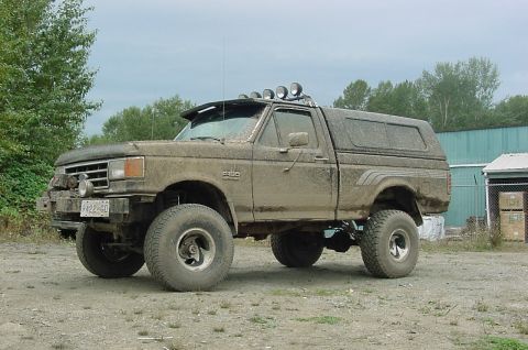 1990 Ford F-150 - This lifted pickup truck is covered in mud and has several auxiliary lights mounted on the roof and bumper.
