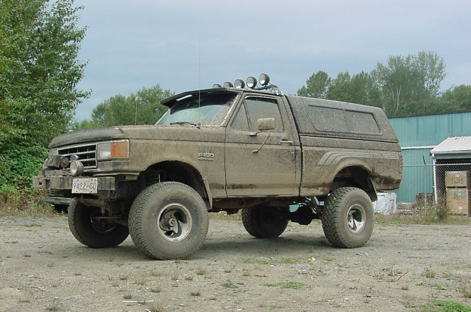 Muddy pickup truck with a camper shell and off-road lights. License plate reads 6422-GO