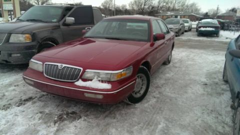 2000 Mercury Grand Marquis - A red sedan sits in a snowy lot next to a dark pickup truck.