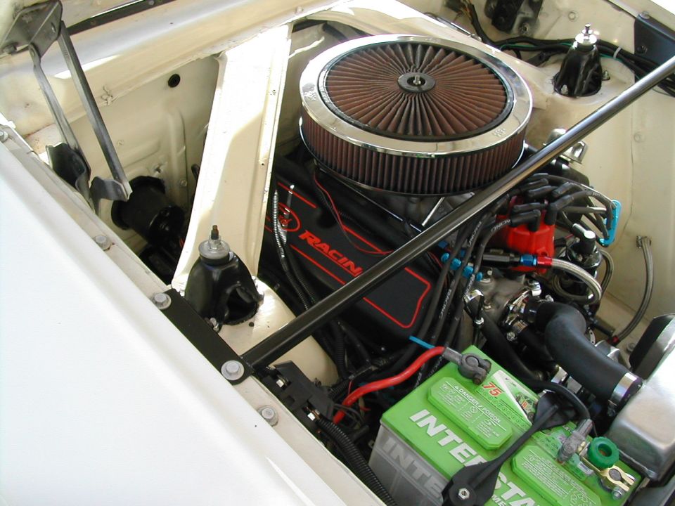 White car engine bay with a large air filter, red racing valve covers, and a green Interstate battery