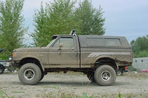 1990 Ford F-150 - This mud-caked 1990 Ford F-150 pickup truck is seen from the side, equipped with a camper shell and off-road tires.