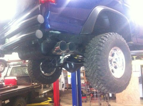 1982 Ford Bronco - The underside of a blue SUV is shown on a lift, highlighting its dual exhaust system and heavy-duty tires.
