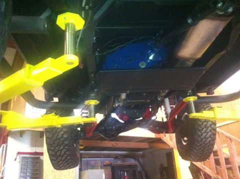 1982 Ford Bronco - The underside of a vehicle is visible, supported by a yellow hydraulic lift, revealing its suspension and mechanical parts.