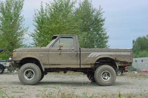 1990 Ford F-150 - Mud-covered 1990 Ford F-150 pickup truck with lifted suspension and large off-road tires.