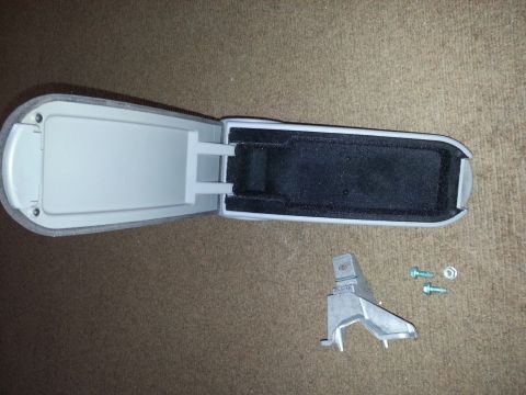 2002 Volkswagen Jetta - A car's center console armrest compartment is shown open, with a detached metal bracket and hardware nearby.