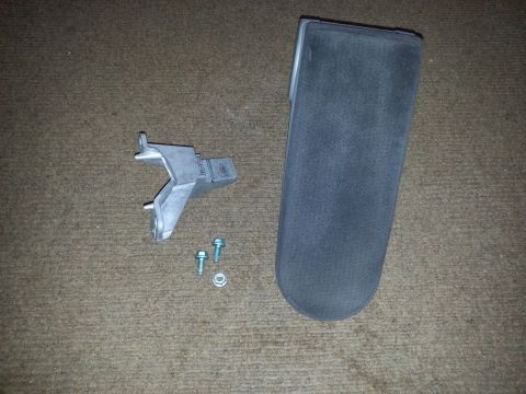 2002 Volkswagen Jetta - A metal bracket, two bolts, and a dark gray car part are laid out on a textured surface.