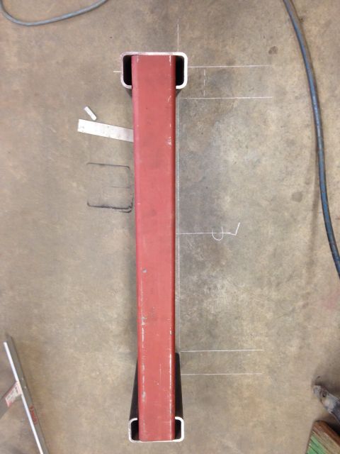 1993 Ford Bronco - A red metal part with white chalk markings and black end caps is shown on a concrete floor.