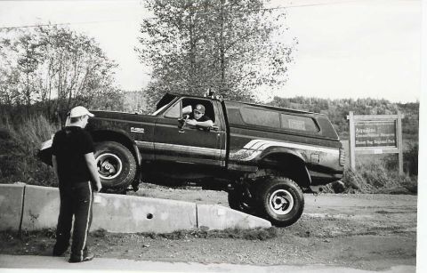 1990 Ford F-150 - A Ford F-150 pickup truck is positioned on a concrete barrier, with a person visible in the driver's seat.