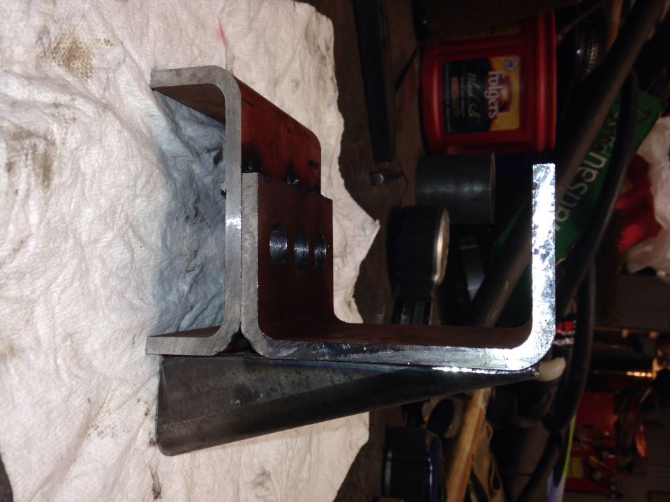 Metal bracket with three bolt holes, resting on paper towels next to oil and tools