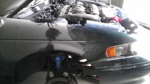 1993 Ford Taurus - Front passenger side of a car with the hood open, showing the engine and fender with primer.