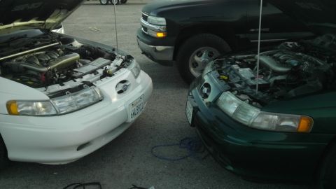 1993 Ford Taurus - Two Ford Taurus cars with hoods open, parked alongside a black pickup truck.