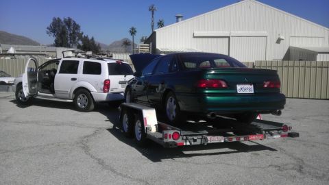 1993 Ford Taurus - A green sedan is being towed on a trailer, with a white SUV parked nearby.