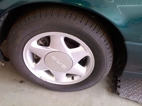 1993 Ford Taurus - Close-up of a green car's wheel, a five-spoke rim and a center cap with a simple three-line emblem.